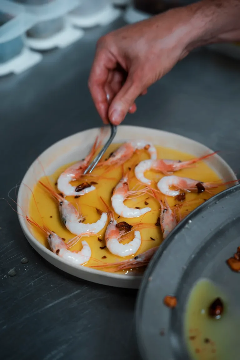 Mano terminando un plato con salsa anaranjada y piezas rosadas y blancas